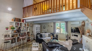 A spacious living area with a black leather sofa, a wooden staircase, and a bookshelf filled with books and decorative items.