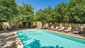 A swimming pool with lounge chairs and a small building, surrounded by trees.