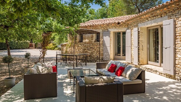 A stone house with a tiled roof, a patio with wicker furniture, and a stone wall.