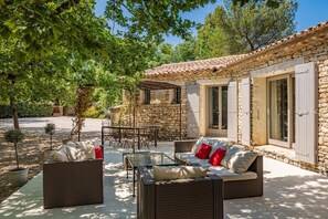 A stone house with a tiled roof, a patio with wicker furniture, and a stone wall. - GORDES Private house and heated swimming pool on enclosed land planted with trees (Gordes)