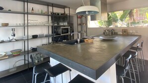 A modern kitchen with a central island, bar stools, and a variety of kitchenware on shelves. - Your Exceptional Getaway in Le Grau-d'Agde: Architect-Designed Villa with Private Pool (Agde)