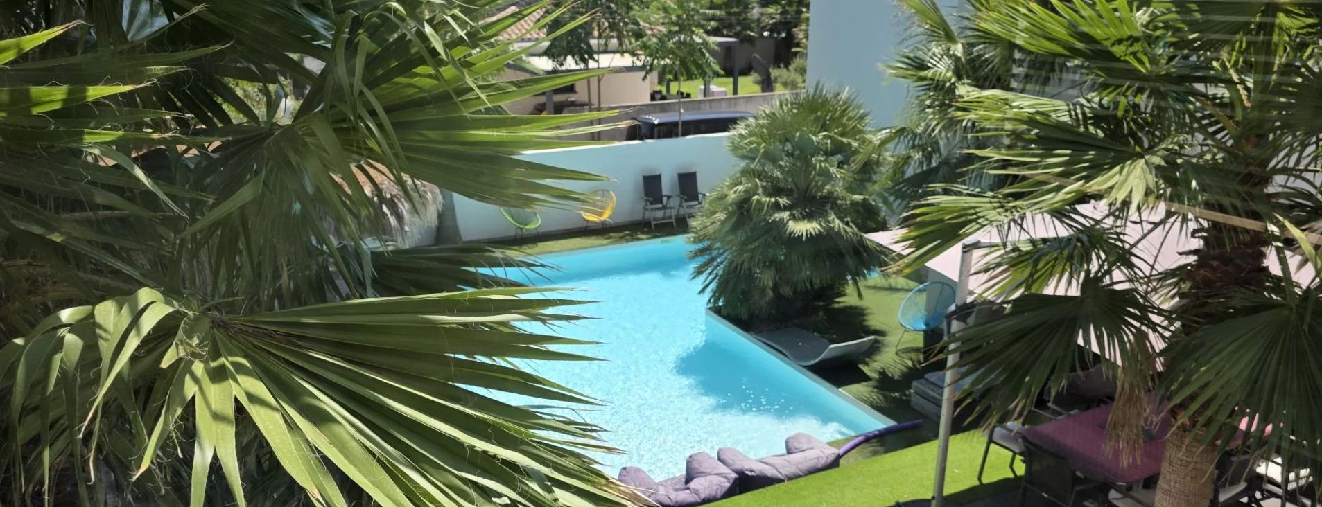 A swimming pool surrounded by palm trees and a white building with a flat roof.