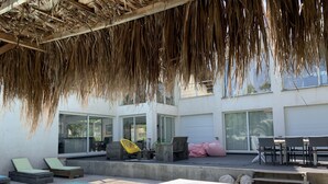 A poolside area with a wooden deck, lounge chairs, a bed, and a thatched roof. - Your Exceptional Getaway in Le Grau-d'Agde: Architect-Designed Villa with Private Pool (Agde)