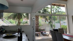 A modern kitchen with large windows, a dining area with outdoor seating, and a view of a garden with palm trees. - Your Exceptional Getaway in Le Grau-d'Agde: Architect-Designed Villa with Private Pool (Agde)