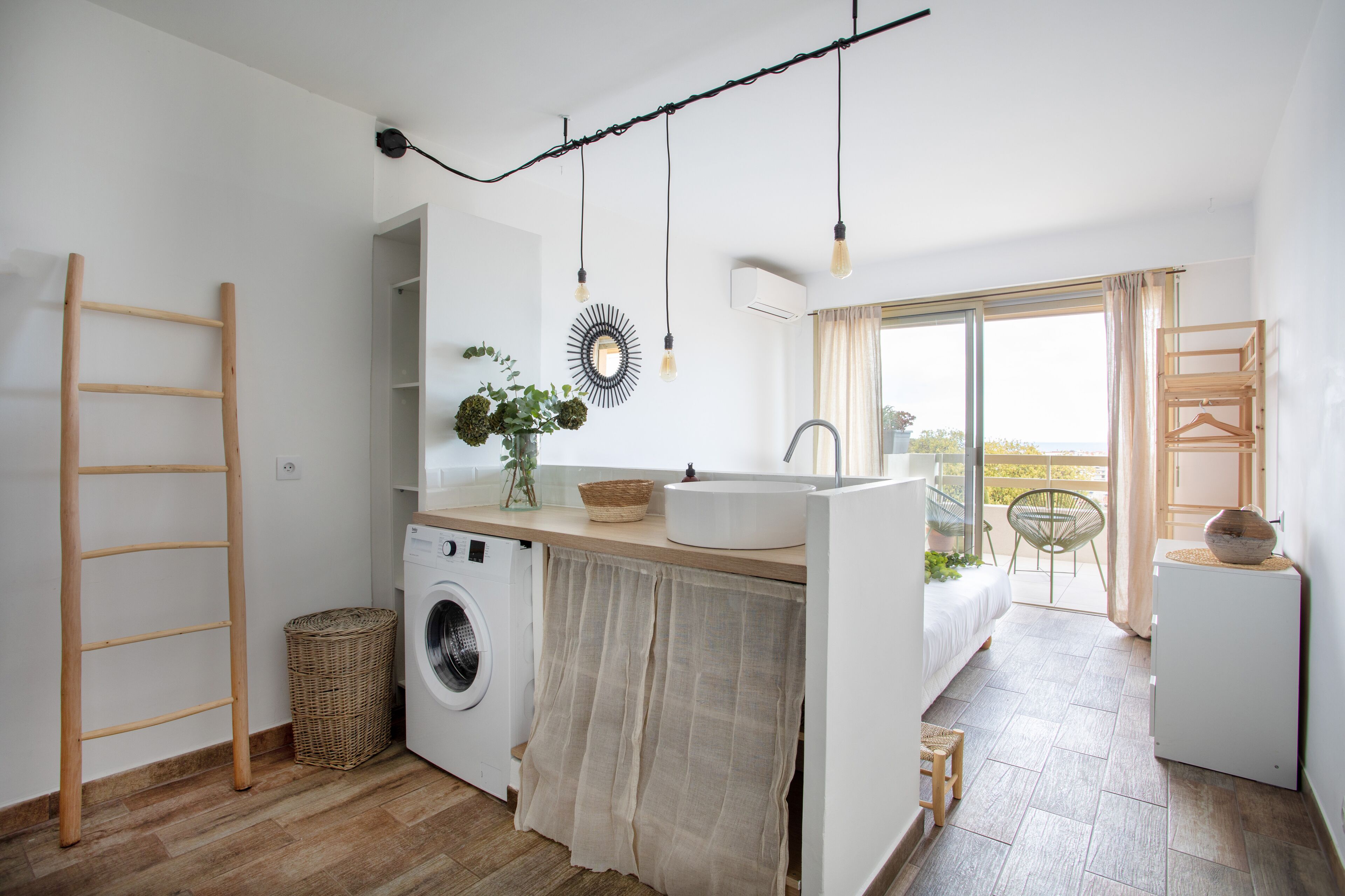 A modern kitchen with a washing machine, wooden ladder, and a view to the outside.