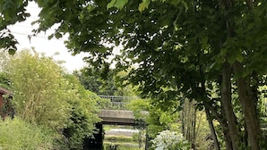 Ein friedlicher Garten mit einem Kanal, üppigem Grün und einer Brücke im Hintergrund.