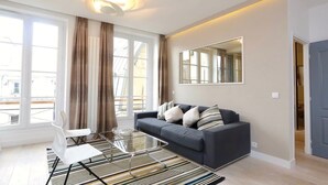 Ein modernes Wohnzimmer mit einer Couch, einem Glastisch und einem großen Fenster mit Vorhängen.