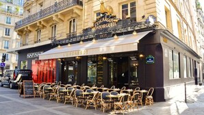 Ein Café mit Außenbereich, einem alten Schild und klassischer europäischer Architektur.
