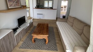 A living room with a wooden coffee table, a sofa, a TV, and a kitchen in the background. - FRONT DE MER, 50 m² LUXUEUX, 4 Personnes, Beach at 50m, TERRACE of 80m², 3 beds (Carry-Le-Rouet)