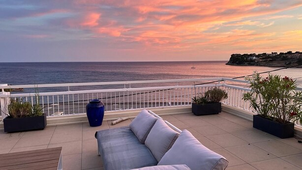 A balcony with a sofa and potted plants, overlooking a coastal view with a sunset. - FRONT DE MER, 50 m² LUXUEUX, 4 Personnes, Beach at 50m, TERRACE of 80m², 3 beds (Carry-Le-Rouet)