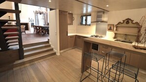 A modern kitchen with a central island, a dining area with a chandelier, and a staircase leading to an upper level.