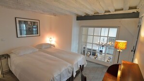 A room with two beds, a window with a view, a lamp, and a wooden bench.