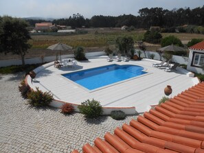 Une piscine dotée d’une terrasse carrelée, entourée de chaises longues et de parasols, le tout dans un cadre rural.