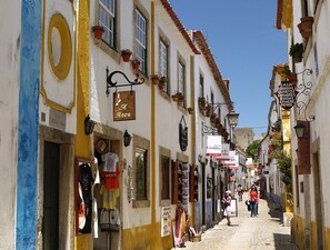 Una calle estrecha flanqueada por edificios, algunos con letreros que indican habitaciones en alquiler.