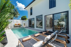 A modern house with a swimming pool, sun loungers, and a glass door leading to a patio.