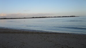 A beach with a calm sea, a sandy shore, and a distant shoreline with buildings. - Bright and comfortable house in a quiet area in a wooded park near the beaches. (Plouharnel)