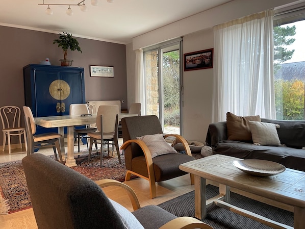 Un salón acogedor con sofá, sillas, una mesa de comedor y un ventanal con cortinas.