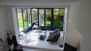 A modern living room with a large glass door leading to a garden. There are two sofas, a coffee table, and a TV. - HOUSE WITH HEATED SWIMMING POOL 50 M FROM ANDERNOS BEACH (Andernos-Les-Bains)