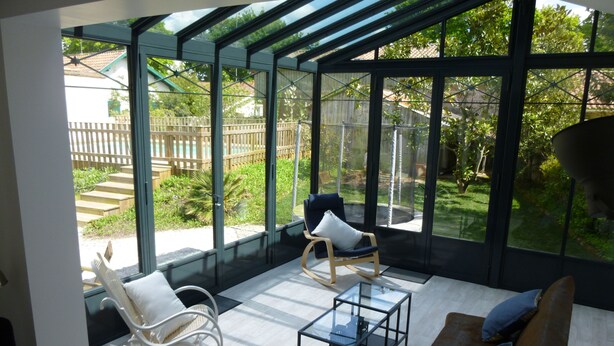 A sunlit room with a glass ceiling, a white rocking chair, a brown sofa, and a glass coffee table. - HOUSE WITH HEATED SWIMMING POOL 50 M FROM ANDERNOS BEACH (Andernos-Les-Bains)