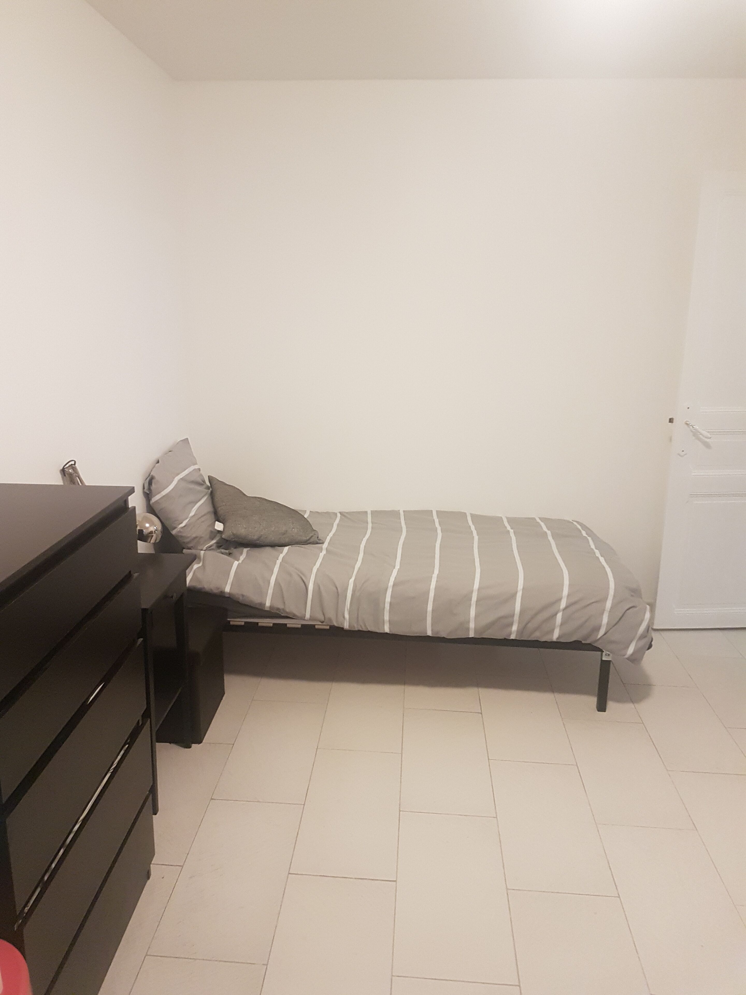 A small, single-bed room with a dark dresser and a door to the right.