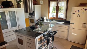 A modern kitchen with a central island, white cabinetry, stainless steel appliances, and a view through the window. - Gîte with SPA in a large park in the heart of Périgord ( Monpazier-Dordogne) (Capdrot)