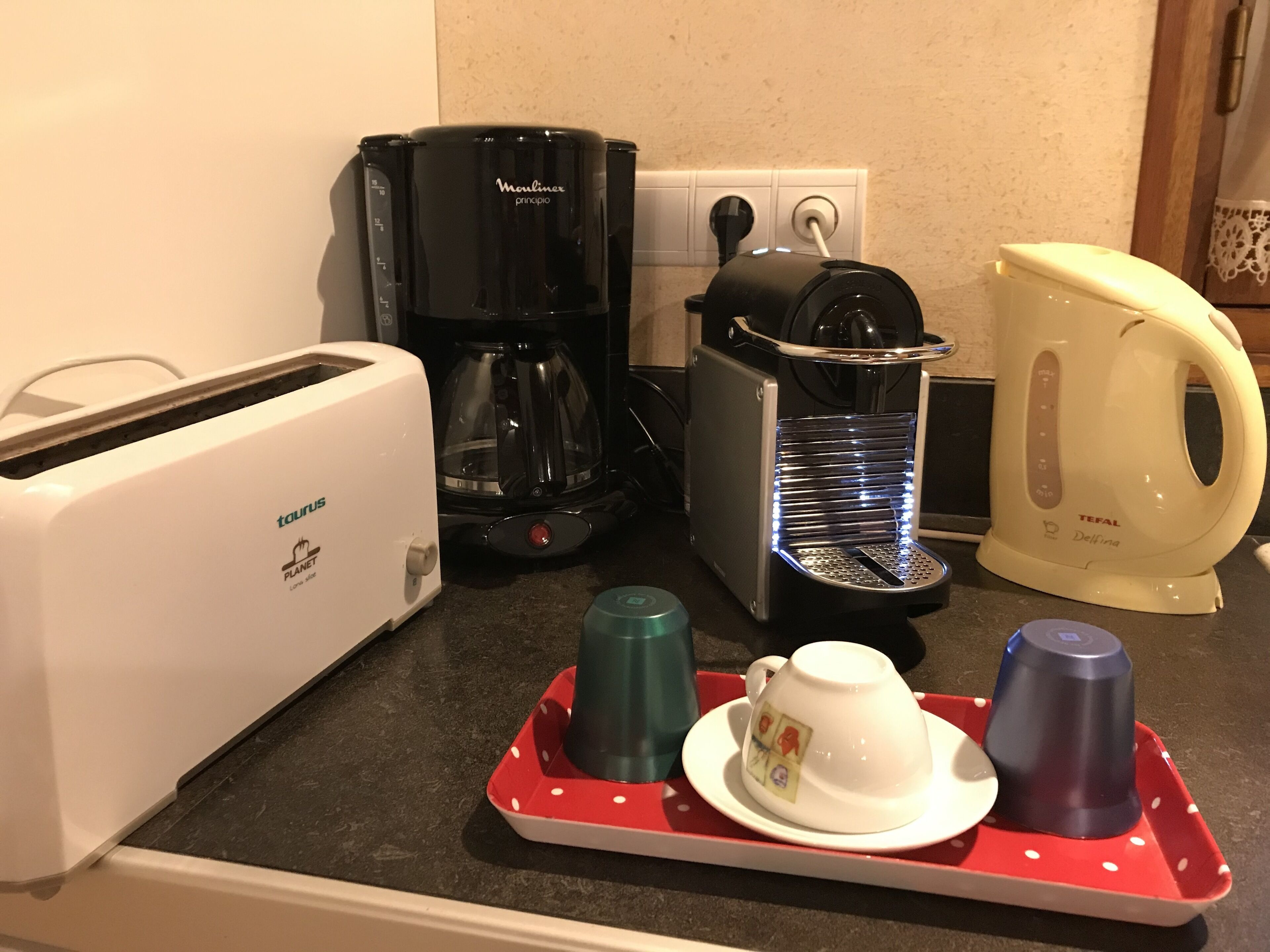 A kitchen counter with a toaster, a coffee maker, a kettle, and a tray with cups and a teapot.