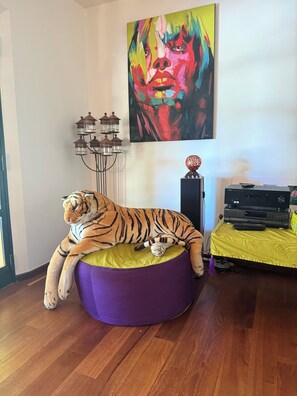 A tiger plush toy on a purple bean bag chair, a television on a stand, and a colorful abstract painting on the wall.
