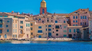 A coastal town with buildings along the waterfront, a prominent tower with a yellow dome, and people on the beach.