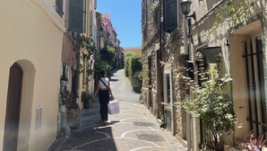 A narrow cobblestone street flanked by historic buildings with shuttered windows and stone facades.
