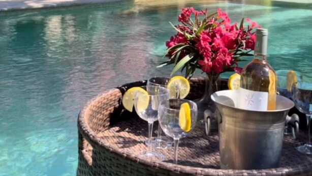A poolside setting with a table set for drinks, a bottle of wine, and a vase of flowers.