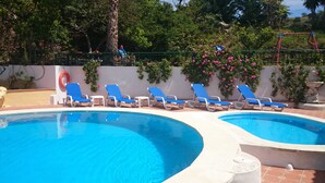 Una piscina con agua azul, rodeada de sillas reclinables blancas y una pared blanca con flores rosas.