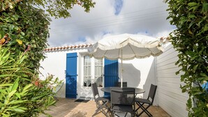 Una terrazza esterna con un tavolo rotondo e quattro sedie, immersa nel verde e protetta da un ombrellone bianco.