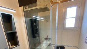 Un bagno moderno con cabina doccia in vetro, lavandino bianco e una piccola finestra.