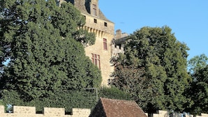 A historic stone building with a prominent tower, surrounded by lush greenery and a stone wall. - "Charming troglodyte house near Sarlat (Vitrac)