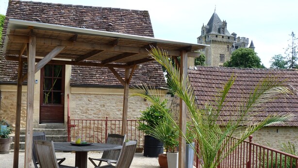 An outdoor patio with a table and chairs, a potted plant, and a stone building with a tower in the background. - "Charming troglodyte house near Sarlat (Vitrac)