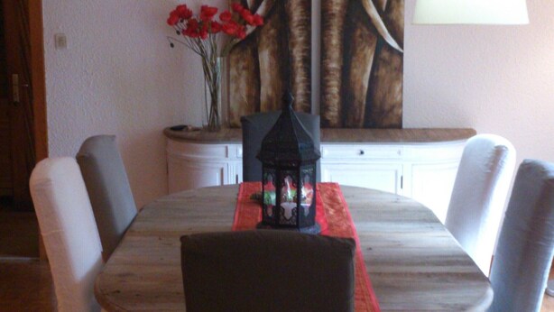 A dining area with a round table, four chairs, a vase with red flowers, and two paintings on the wall. - Large and beautiful wild cottage with sauna Alsace (Mittlach)