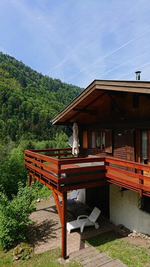 A wooden cabin with a balcony, white lounge chairs, and a view of a forested mountain. - Large and beautiful wild cottage with sauna Alsace (Mittlach)
