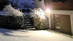 Ein Holzhaus mit Garage, umgeben von schneebedeckten Bäumen und einer Steinmauer.