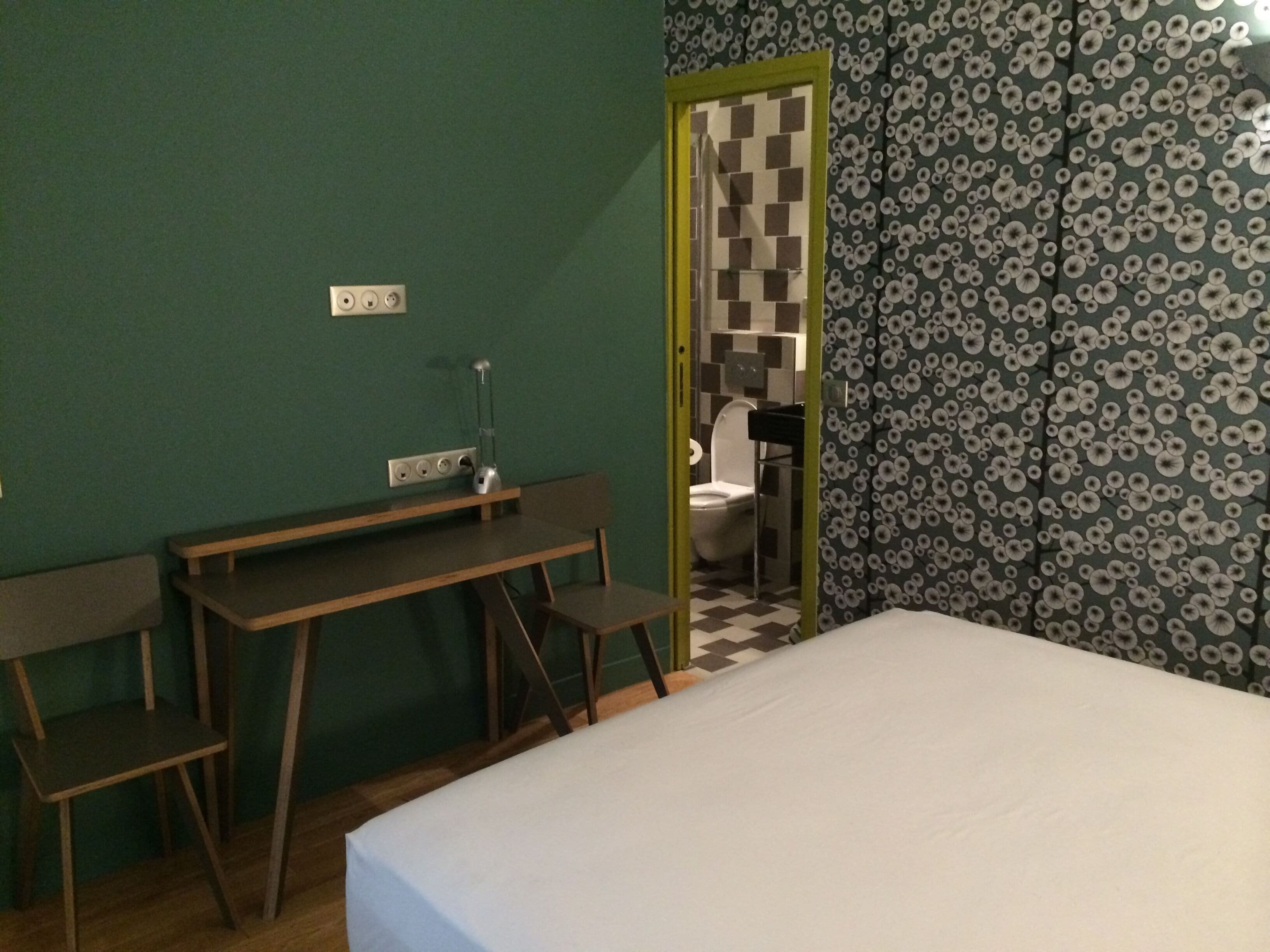 Een kamer met een bed, een bureau en een stoel. Een deur leidt naar een badkamer.