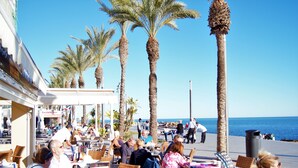 An outdoor dining area with tables and chairs, palm trees, and a view of the sea. - Cozy bungalow, 2 min walk from the beach. Wi-Fi (Torrevieja)