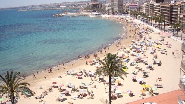 A beach with numerous umbrellas and people, a clear blue sea, and buildings in the background. - Cozy bungalow, 2 min walk from the beach. Wi-Fi (Torrevieja)