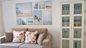A living room with a beige sofa, floral cushions, and a glass cabinet with decorative items. - Cozy bungalow, 2 min walk from the beach. Wi-Fi (Torrevieja)