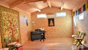 A room with wooden walls and ceiling, a piano, a Buddha statue, and a colorful tapestry.