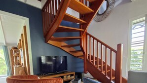 A living room with a wooden staircase, a television, a sofa, and a chair. - SEASONAL RENTAL VILLA STANDING 3/4 PERS (2 ADULT / 2 NFE). POOL SPA SAUNA (Le Moule)
