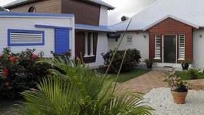 A two-story house with a blue and white exterior, a brown roof, and a brick pathway leading to the entrance. - SEASONAL RENTAL VILLA STANDING 3/4 PERS (2 ADULT / 2 NFE). POOL SPA SAUNA (Le Moule)
