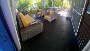 An outdoor covered patio with wicker furniture, a small round table, and a view of greenery. - SEASONAL RENTAL VILLA STANDING 3/4 PERS (2 ADULT / 2 NFE). POOL SPA SAUNA (Le Moule)
