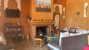 A living room with a fireplace, a television, a bookshelf, and a sofa. - Marrakech Villa for 6-16 people - Exclusive Offer - 450 sq.m and 16 x 5.5 m pool (Marrakech)