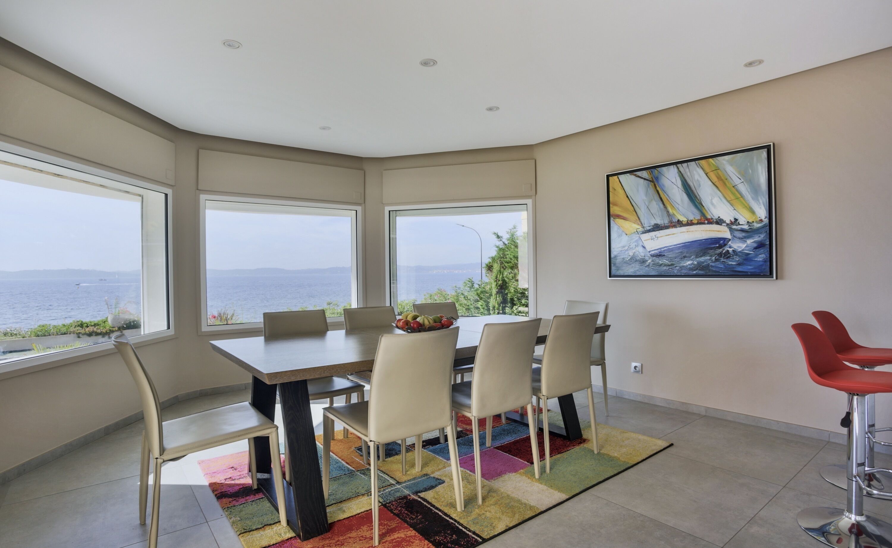A dining area with a table and chairs, a colorful rug, and a painting of a sailboat on the wall.