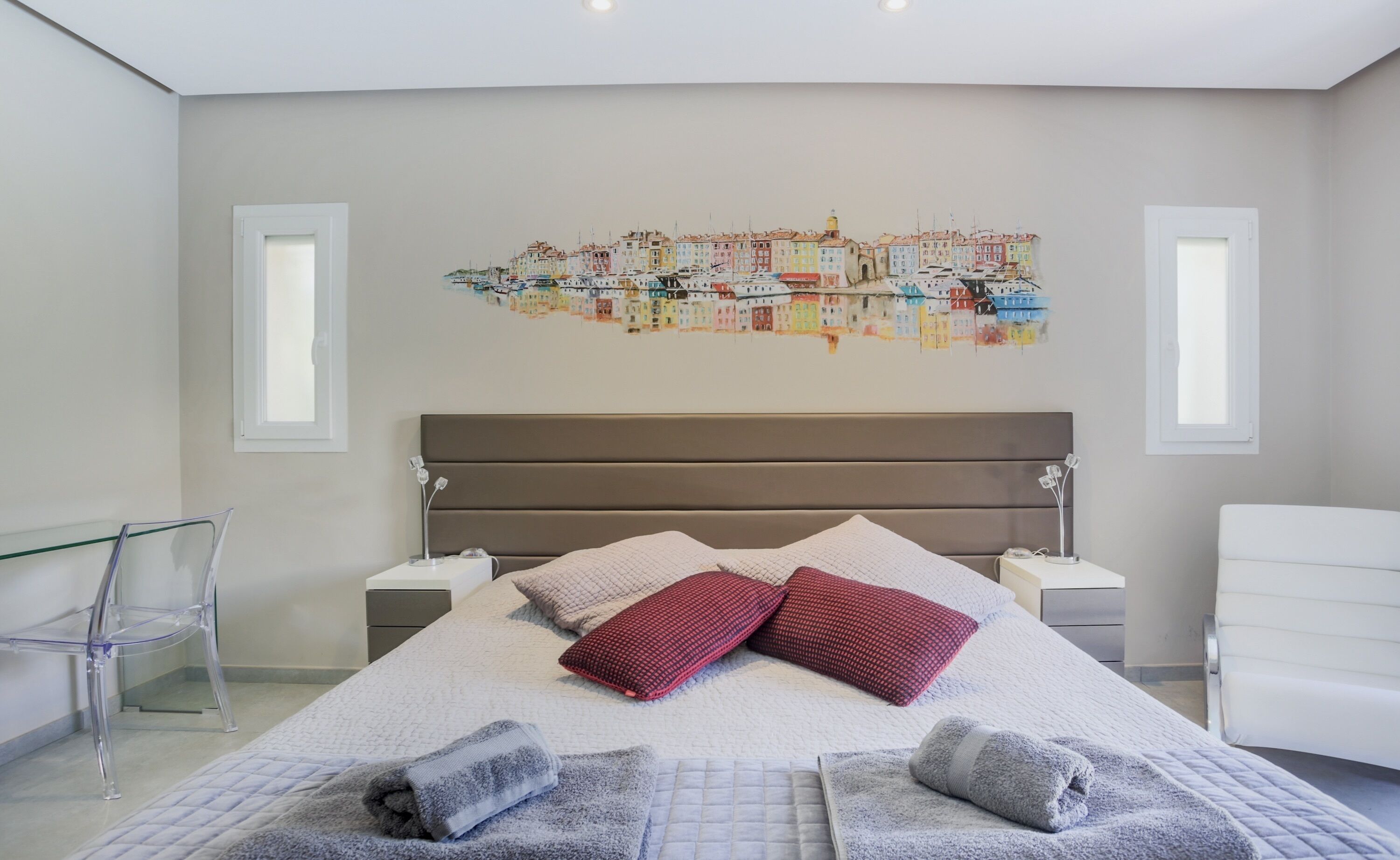 Una camera da letto moderna con un letto grande, due comodini, una poltrona e un murale raffigurante un panorama cittadino.