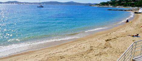 A beach with clear blue water, a boat in the distance, and a staircase leading down to the shore.